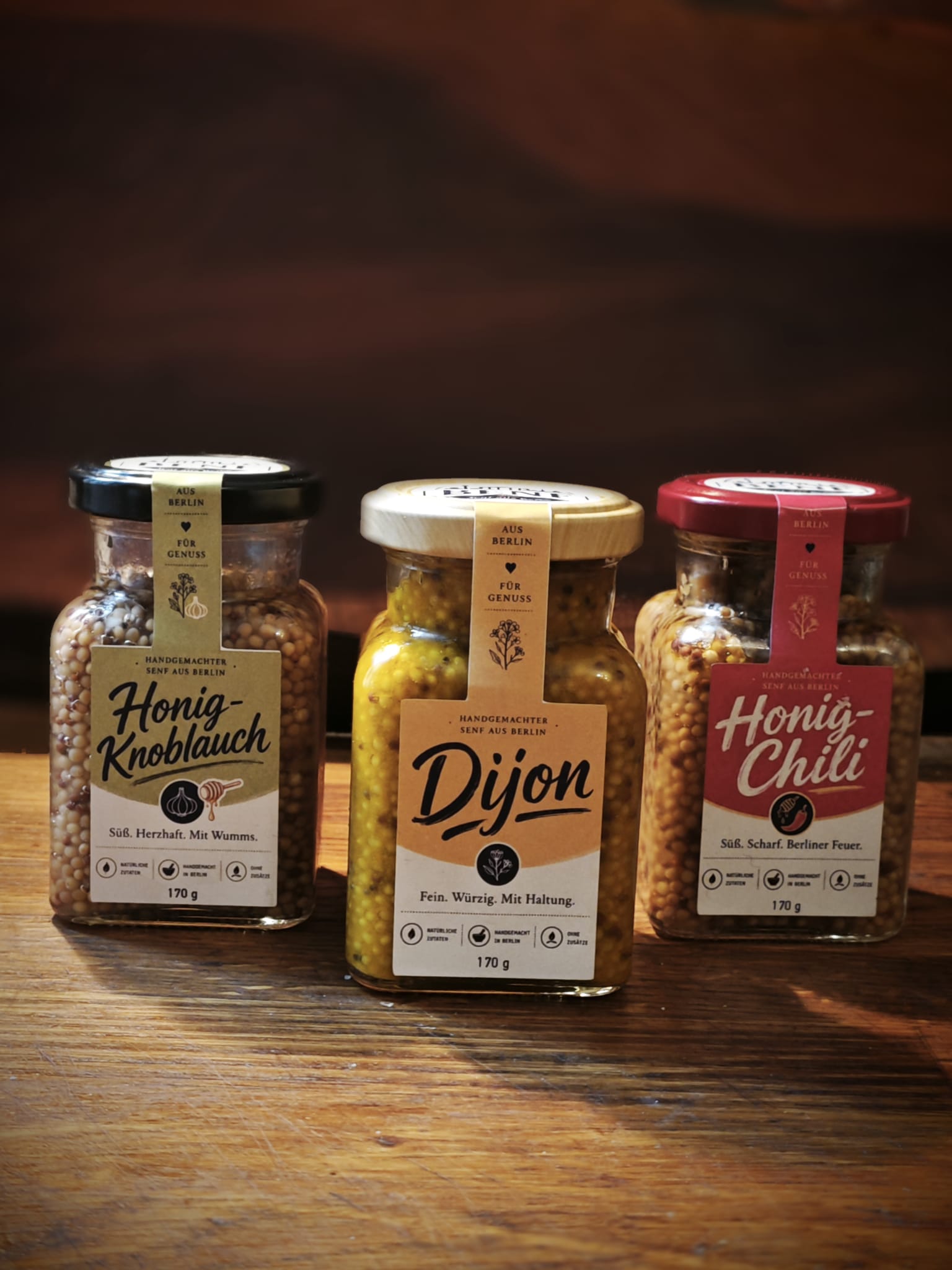 Drei Gläser BENF Senf: Honig-Knoblauch, Dijon und Honig-Chili auf einem Holztisch